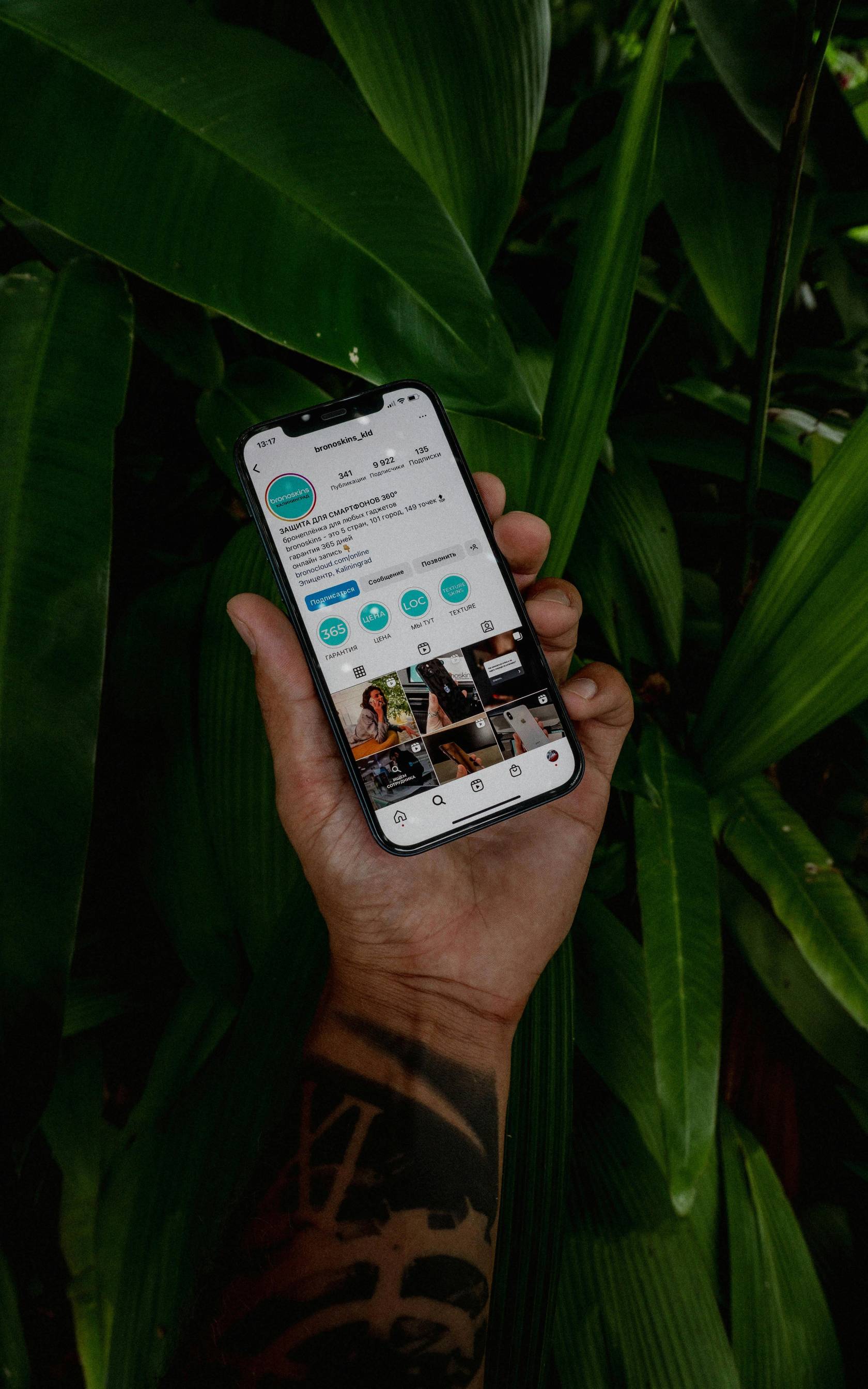 Electronic device displaying an Instagram post promoting smartphone protection services by bronoskins_kld at 13:17, with text in Russian about phone skins, warranty, online booking, and contact information.